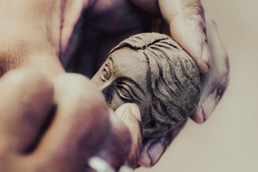 Detailed view of hands crafting a clay face sculpture, showcasing artistic skill.