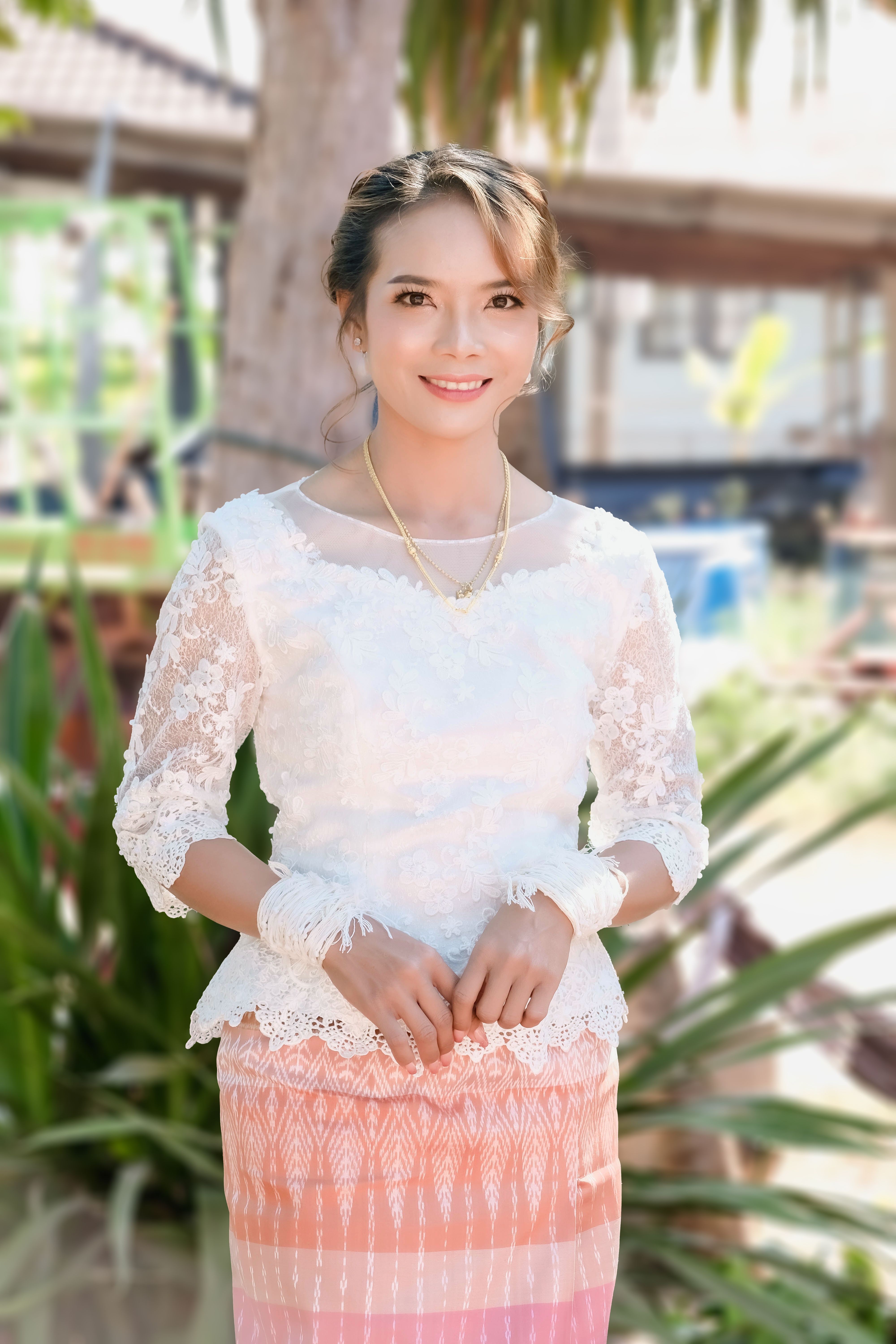 A woman in traditional attire smiles outdoors, exuding warmth and charm on a sunny day.