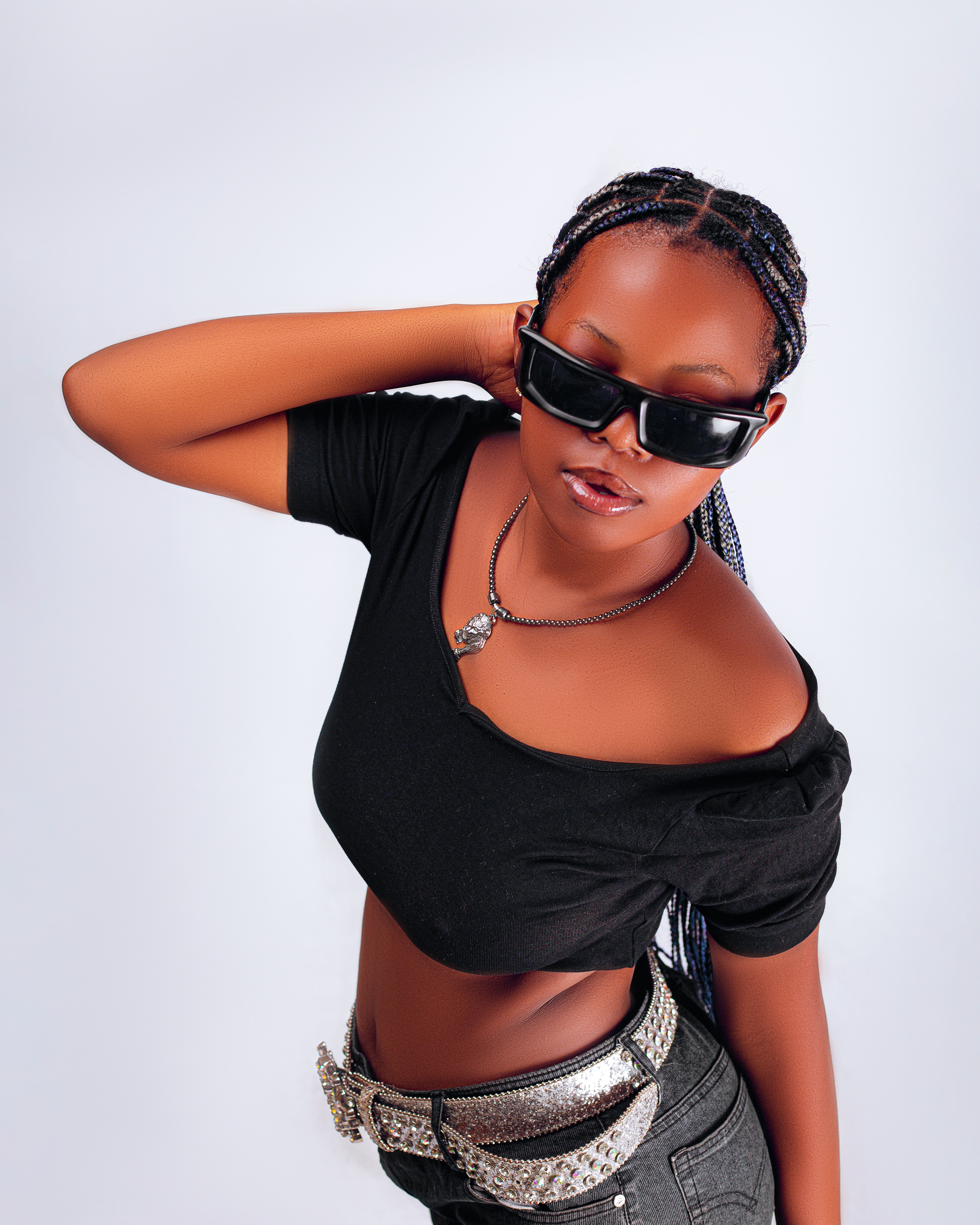 Fashionable young woman posing with sunglasses and braided hair in a striking black outfit.