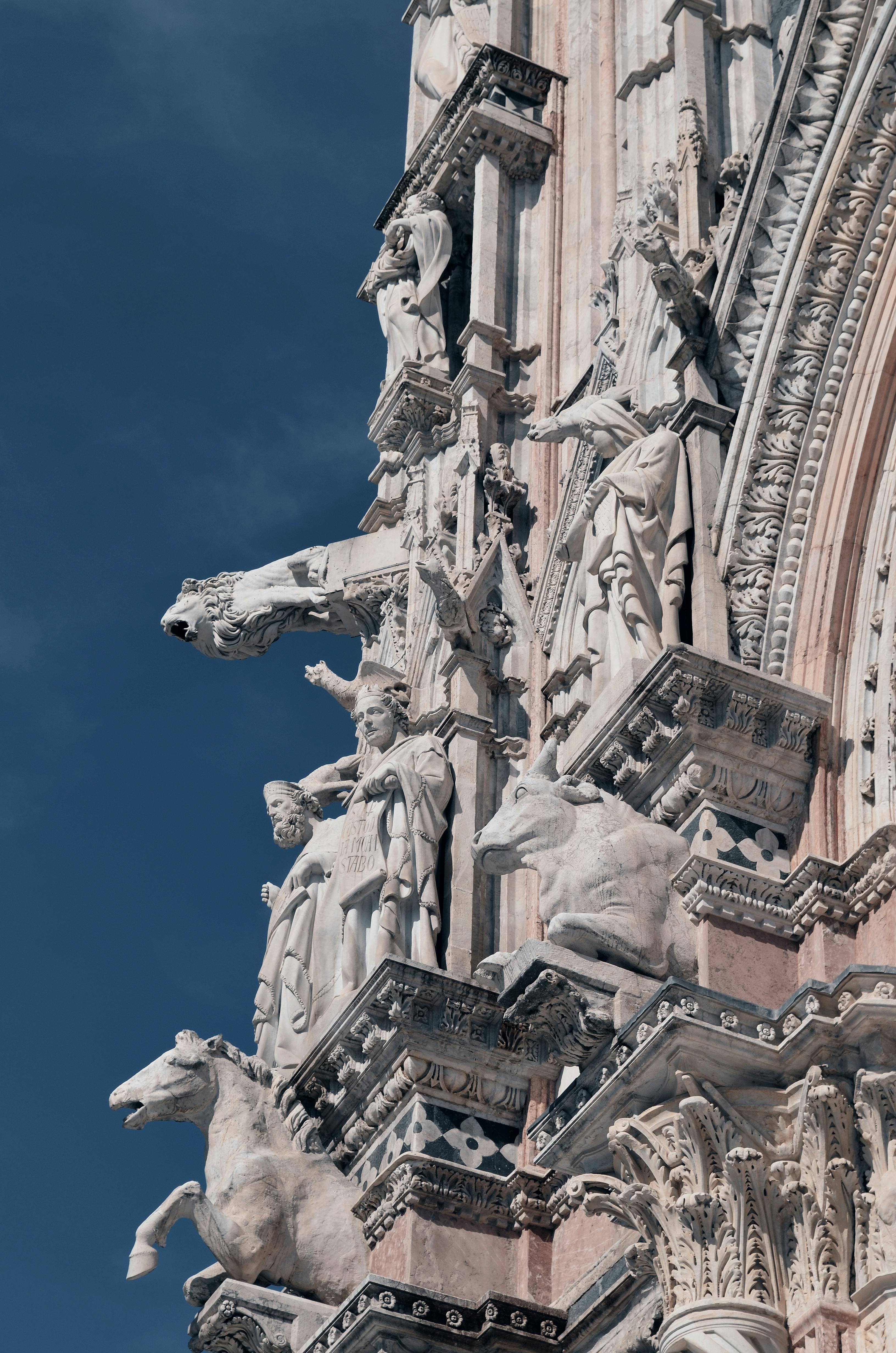Ornate Gothic architecture and sculptures of the Duomo di Siena against a clear blue sky.