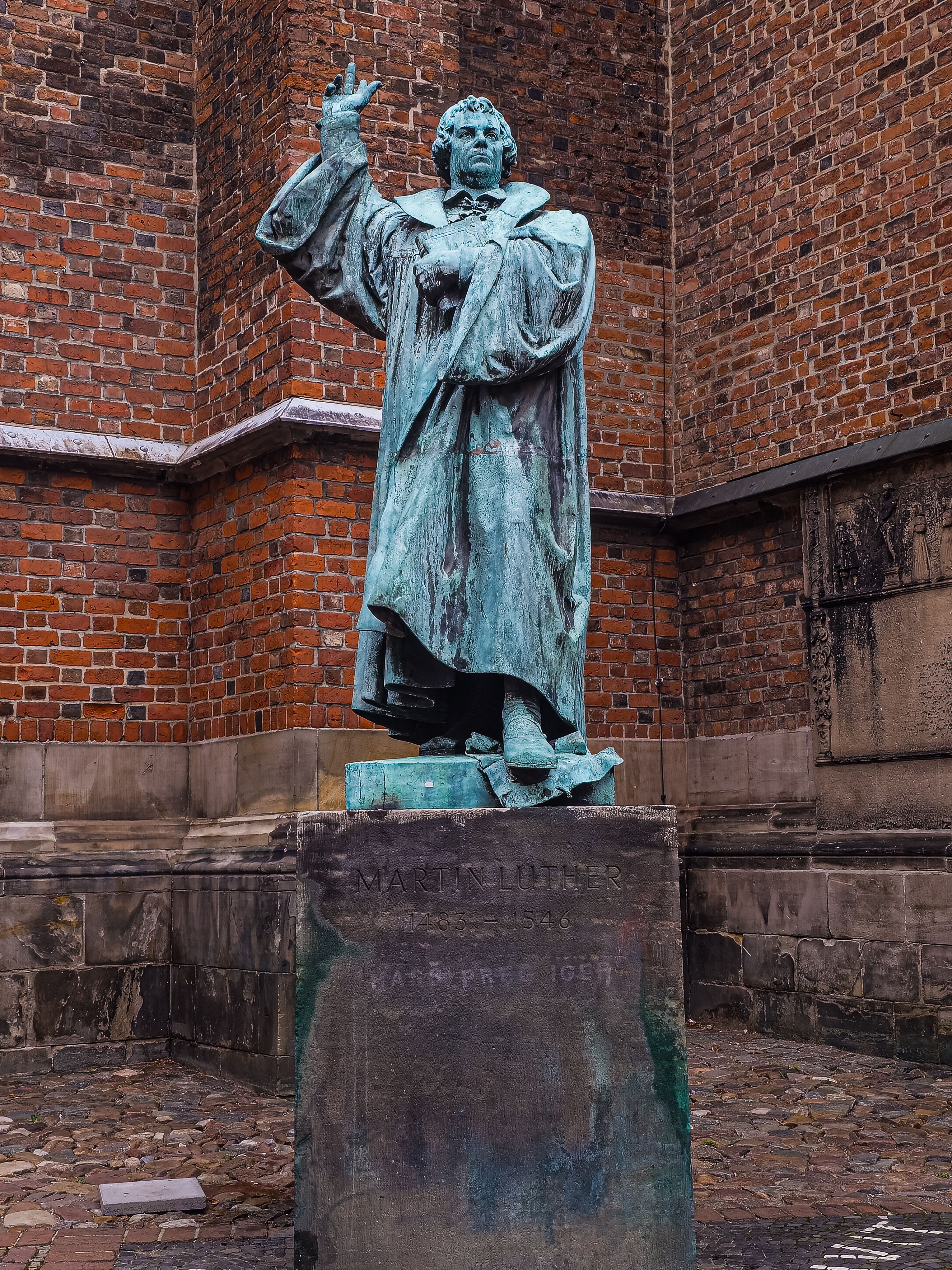 Copper statue in front of brick architecture at St. John's Church, Hannover.