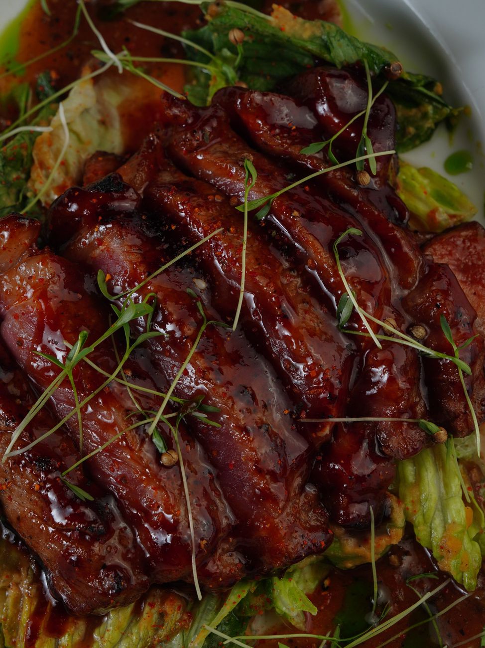 Thick slices of dark, caramelized jerk pork shoulder glazed with golden-brown scotch bonnet sauce, served on a white plate with visible char marks and glossy finish