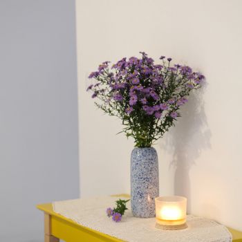 Elegant arrangement of purple flowers in a blue vase next to a glowing candle on a table.