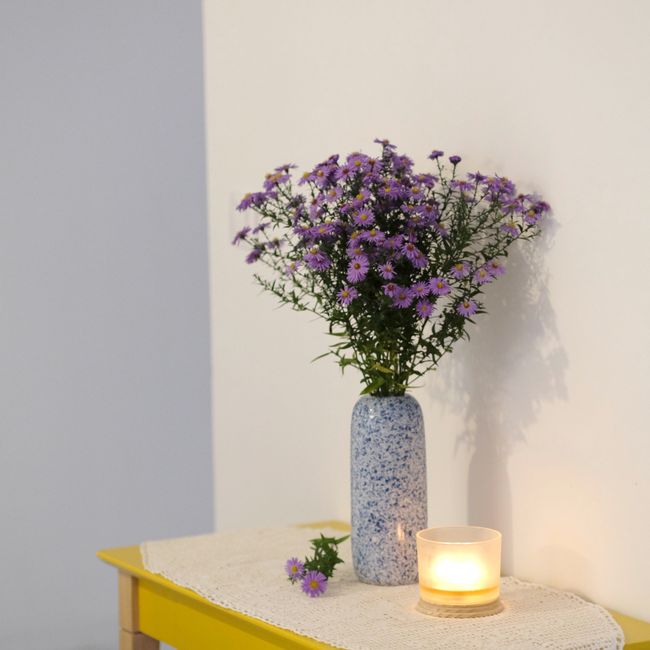 Elegant arrangement of purple flowers in a blue vase next to a glowing candle on a table.