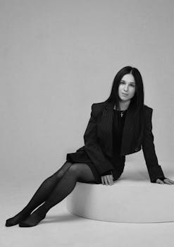 Sophisticated black and white portrait of a young woman in formal attire, sitting gracefully.