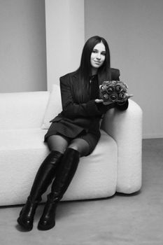 A stylish woman seated on a white sofa holding a decorative object, exuding sophistication.