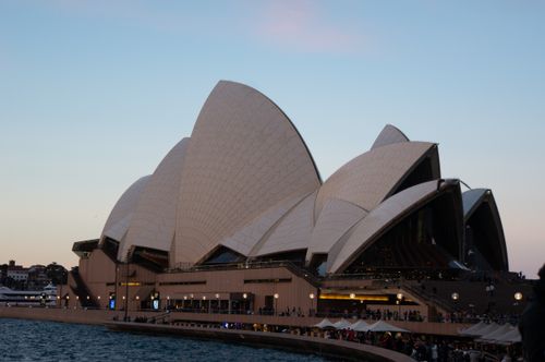 Free Iconic Sydney Opera House photographed at dusk, with lively crowds and serene harbor view. Stock Photo