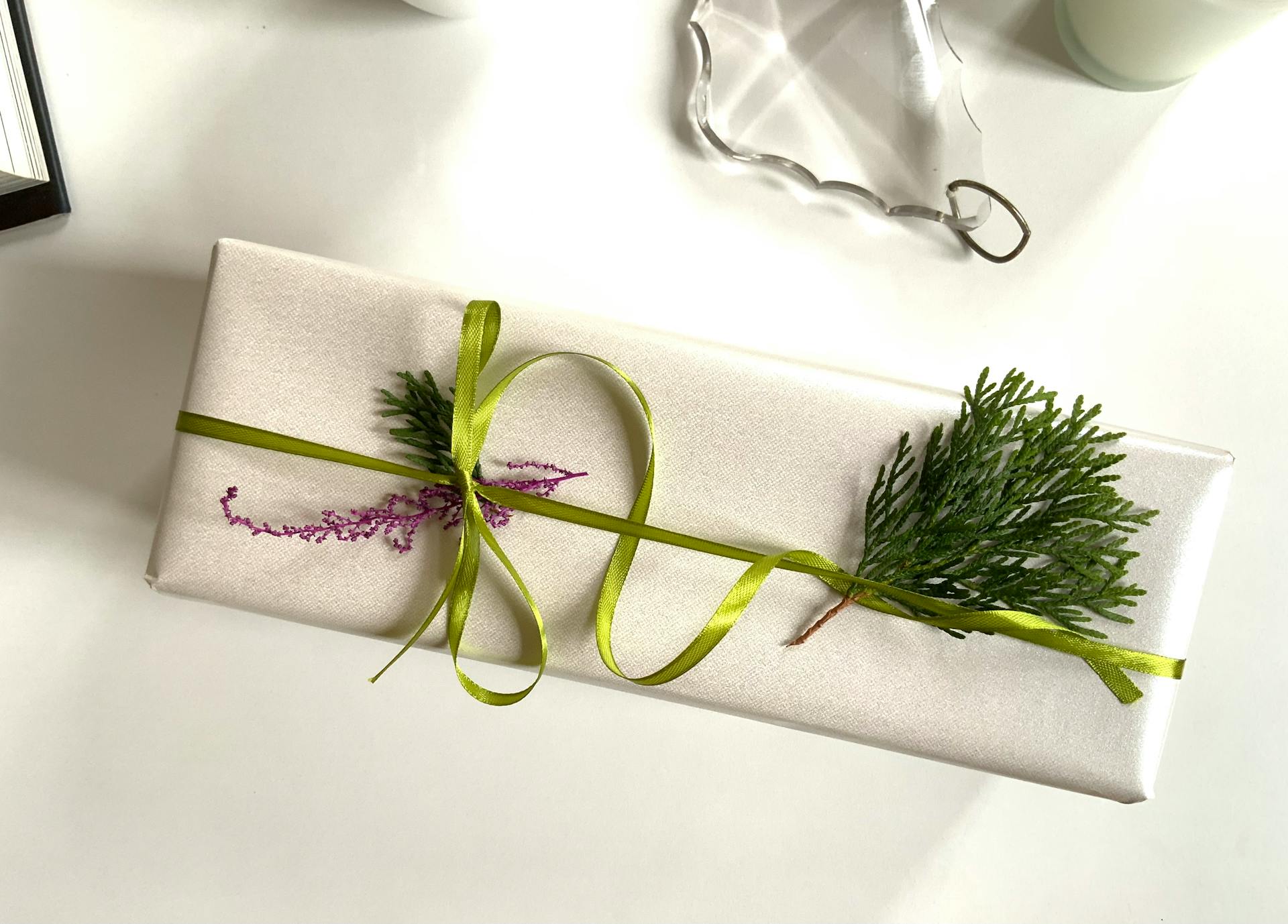 A beautifully wrapped rectangular gift adorned with green ribbon and evergreen sprig, perfect for holidays or celebrations.