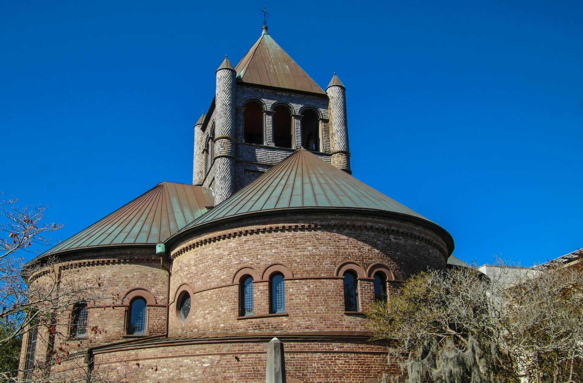 A beautifully preserved round brick church with a copper roof and tower under a clear blue sky.