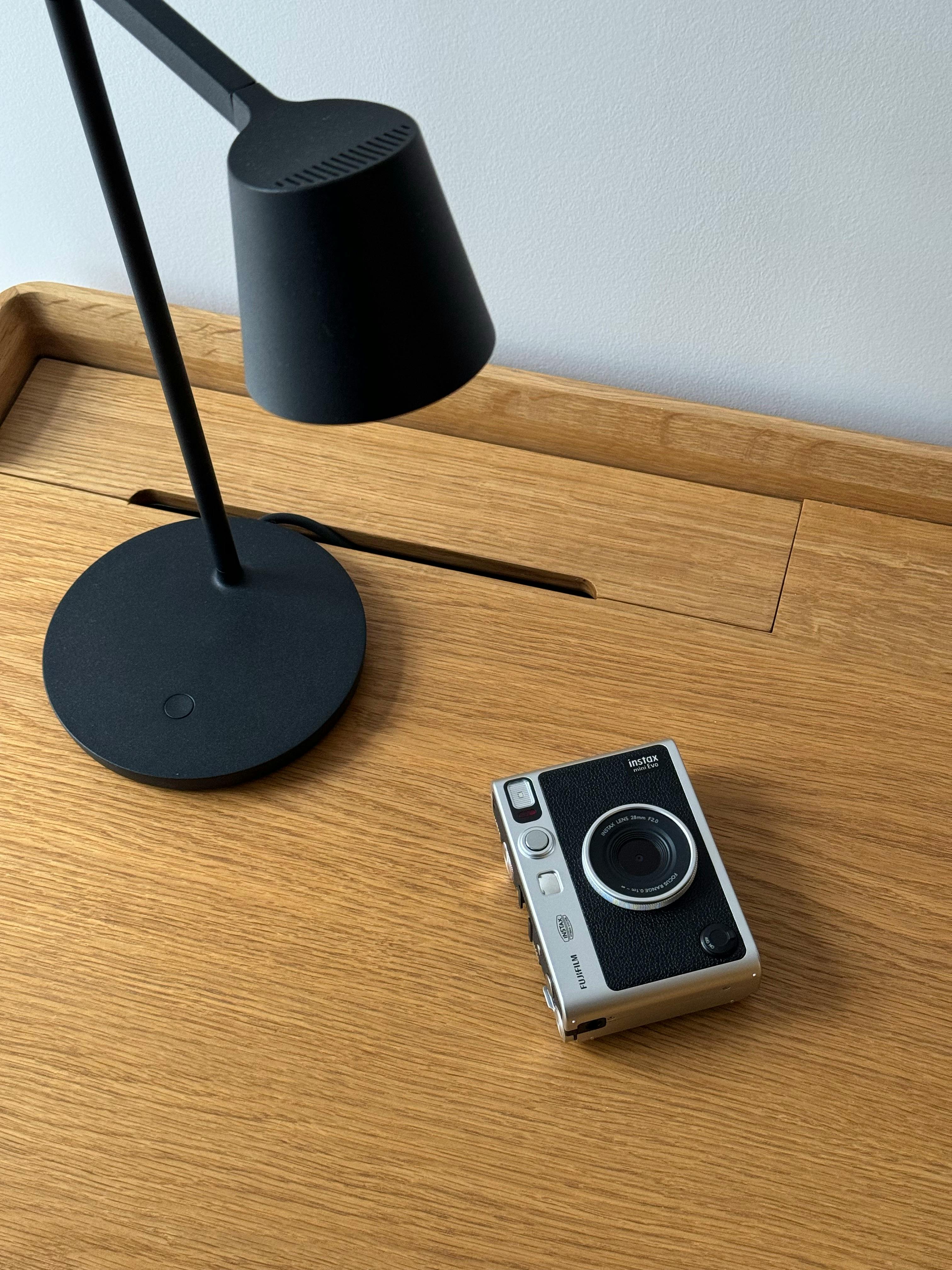 Stylish wooden desk featuring a sleek black lamp and an instant camera.