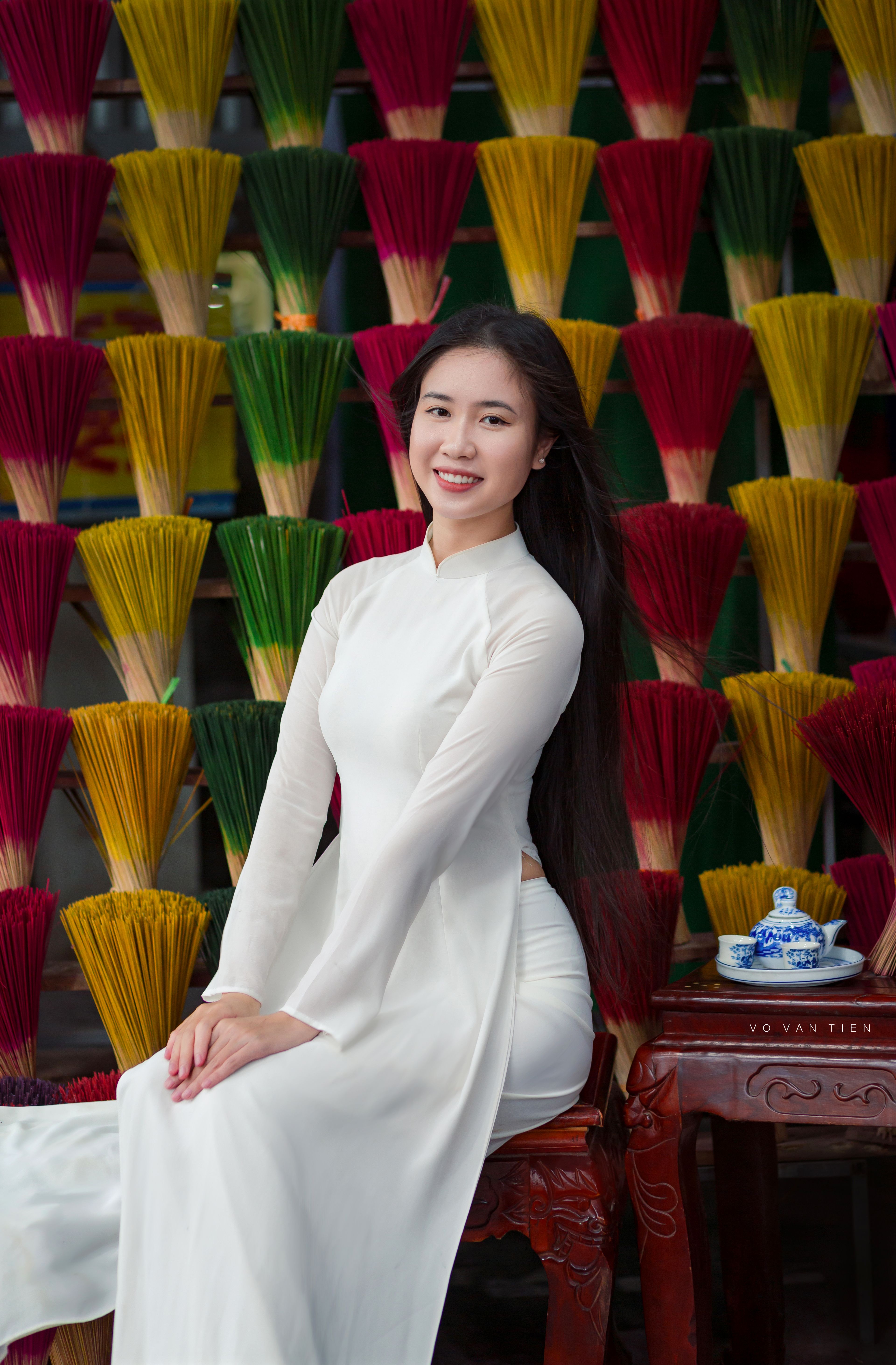 Vietnamese woman in white áo dài poses in front of vibrant incense sticks in Hoi An.