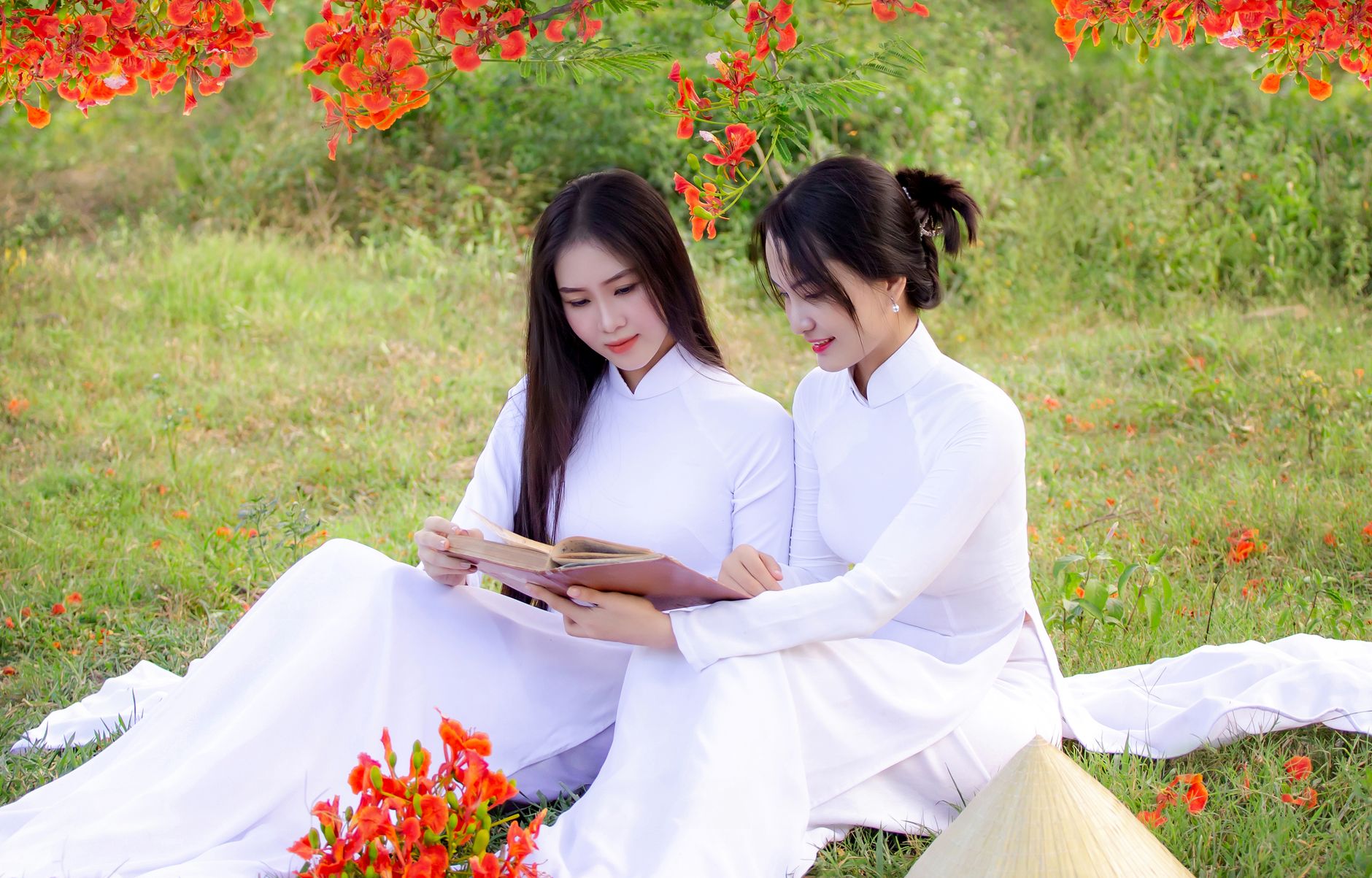 Two women in áo dài reading outdoors in Hội An, Vietnam.