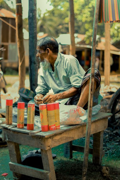 Free Old man selling incense sticks outdoors in a traditional market setting. Stock Photo