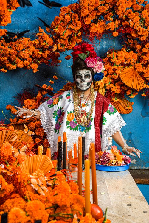 Free Colorful Dia de los Muertos scene featuring a woman in Catrina makeup amid marigold decorations. Stock Photo