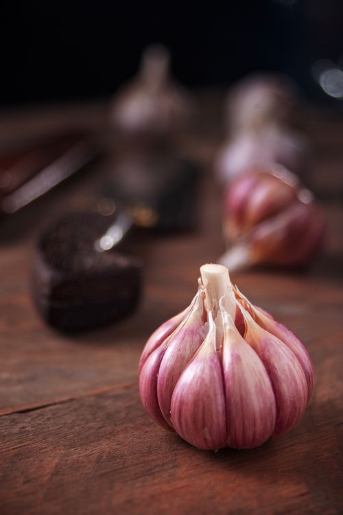 Free Detailed shot of a single garlic bulb on a rustic wooden surface, ideal for culinary themes. Stock Photo