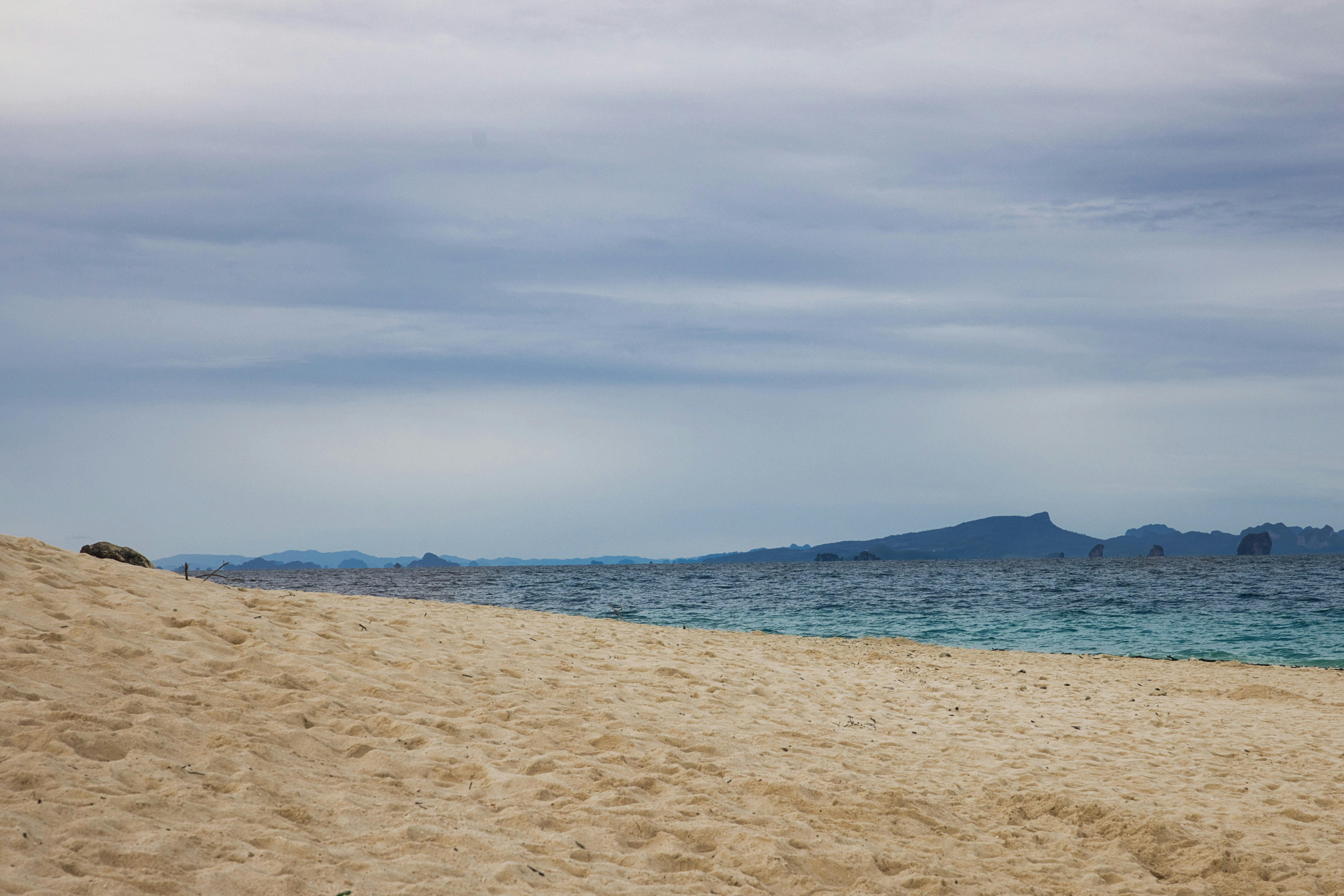 A tranquil sandy beach with clear blue waters and distant islands, photographed in Phuket, Thailand.