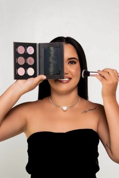 Smiling woman holding makeup palette and brush, showcasing beauty routine.