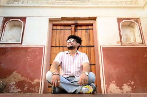 Free Smiling man sitting near a vintage wooden door with ornate historical architecture. Stock Photo