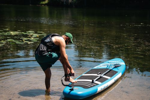 Free A man prepares to paddleboard on a peaceful lake surrounded by nature. Stock Photo