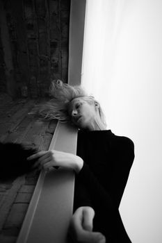 Striking black and white photo of a woman artfully leaning against a wall, capturing emotion and movement.