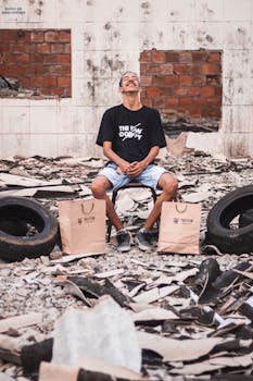 年轻人坐在户外的瓦砾与纸袋旁，面带微笑