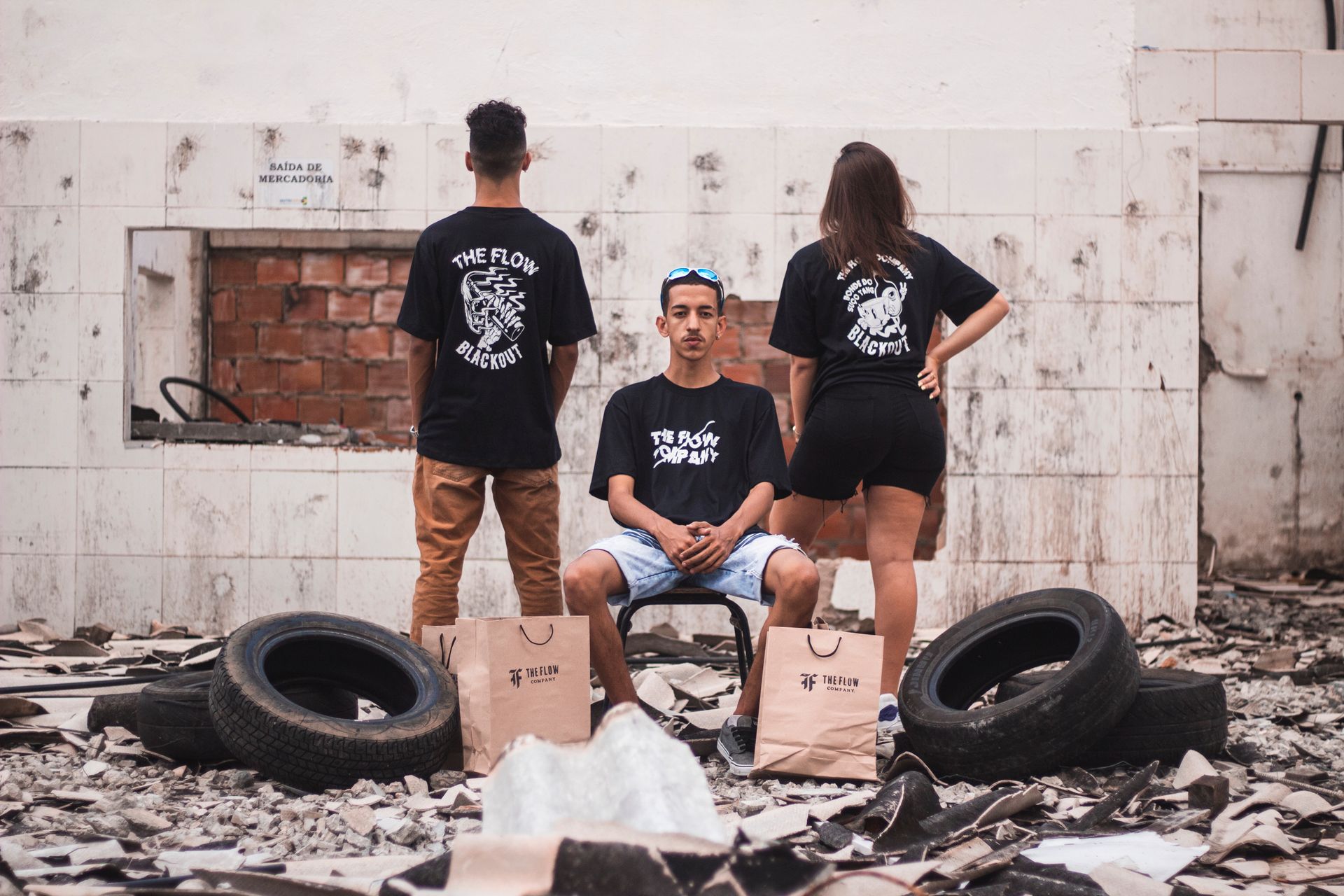 Three adults in an abandoned building, showcasing urban fashion with branded bags.