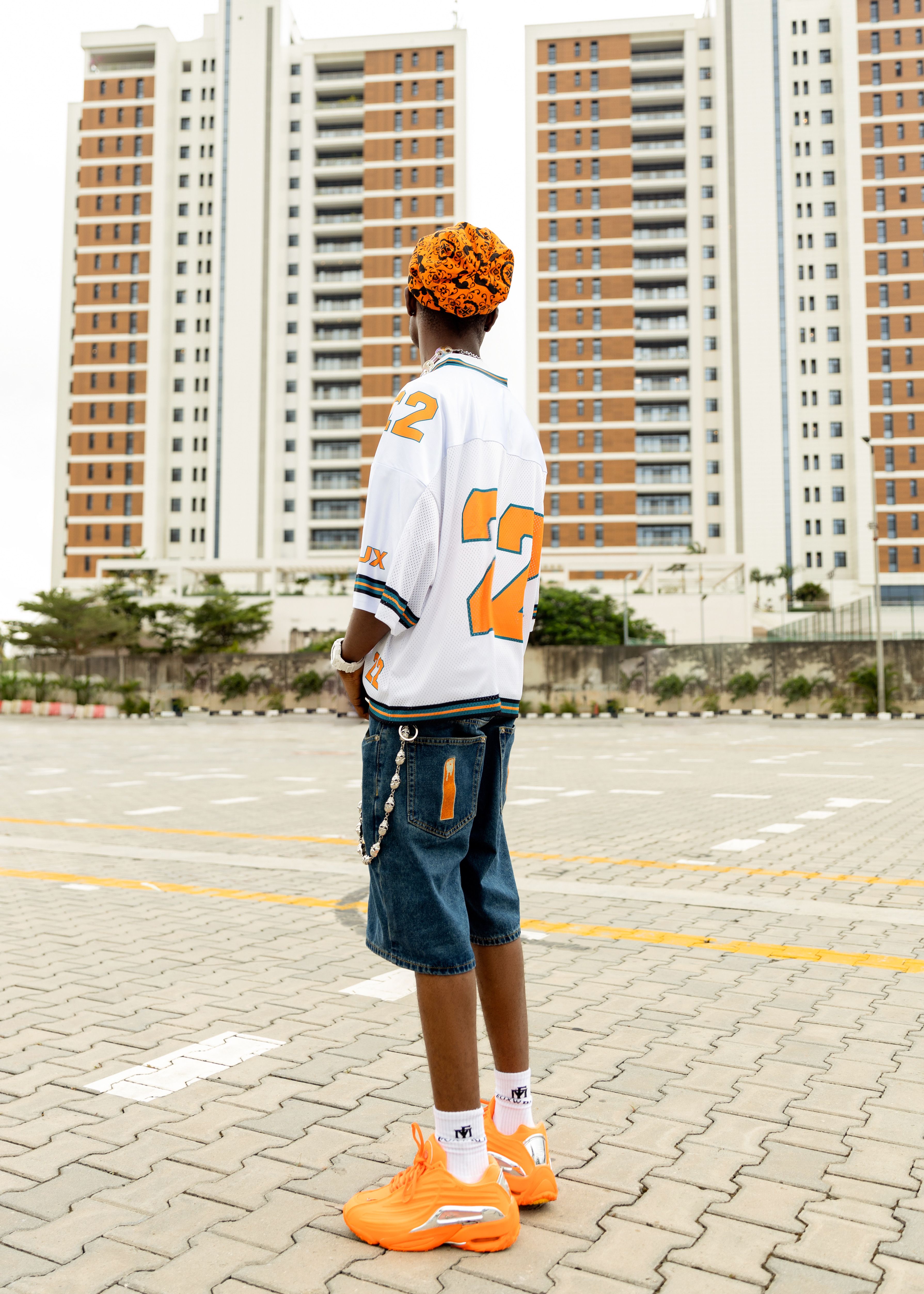 Person in streetwear standing before tall buildings, showcasing modern urban fashion.