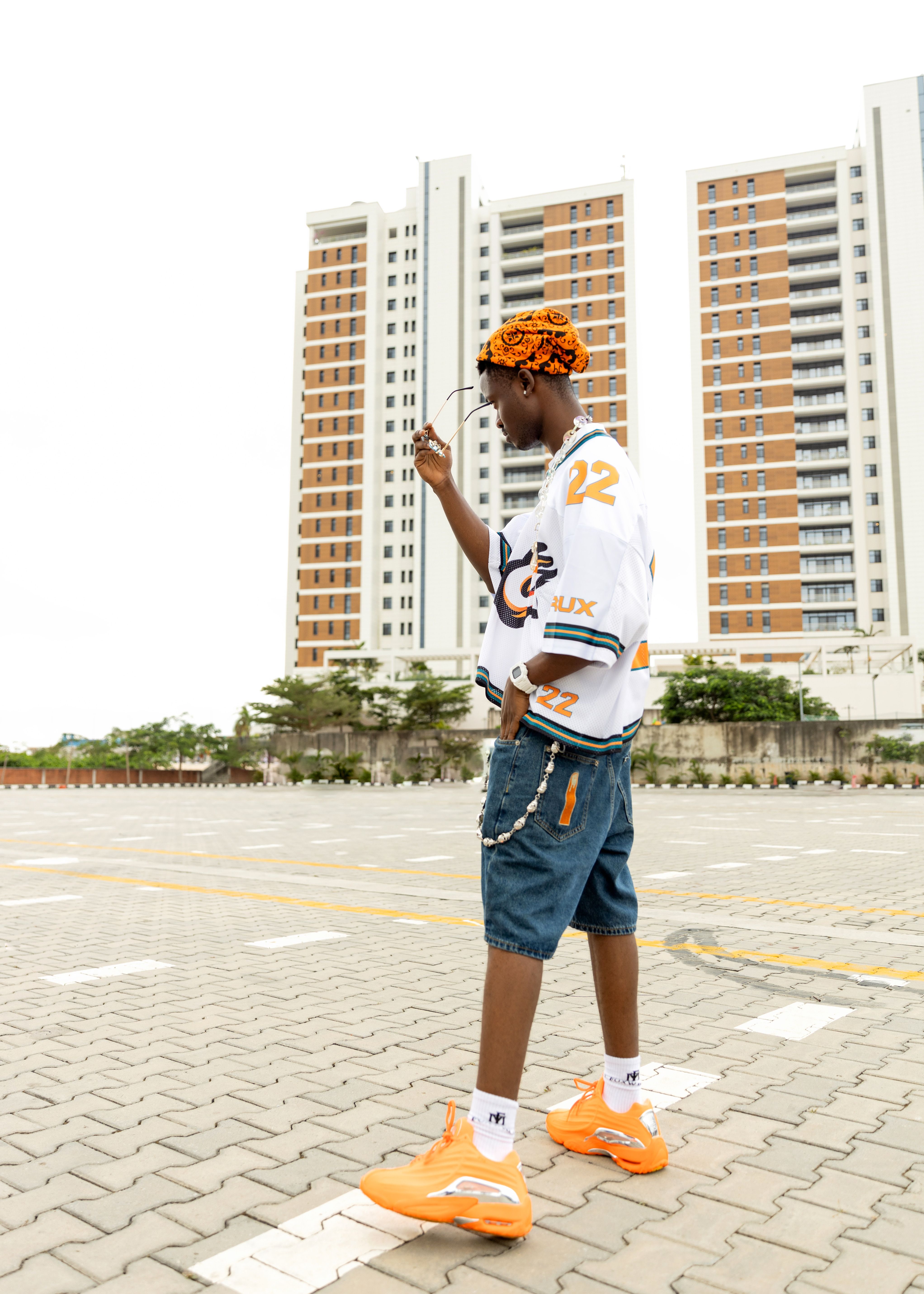 Fashionable young man poses in front of high rise buildings, capturing urban street style.