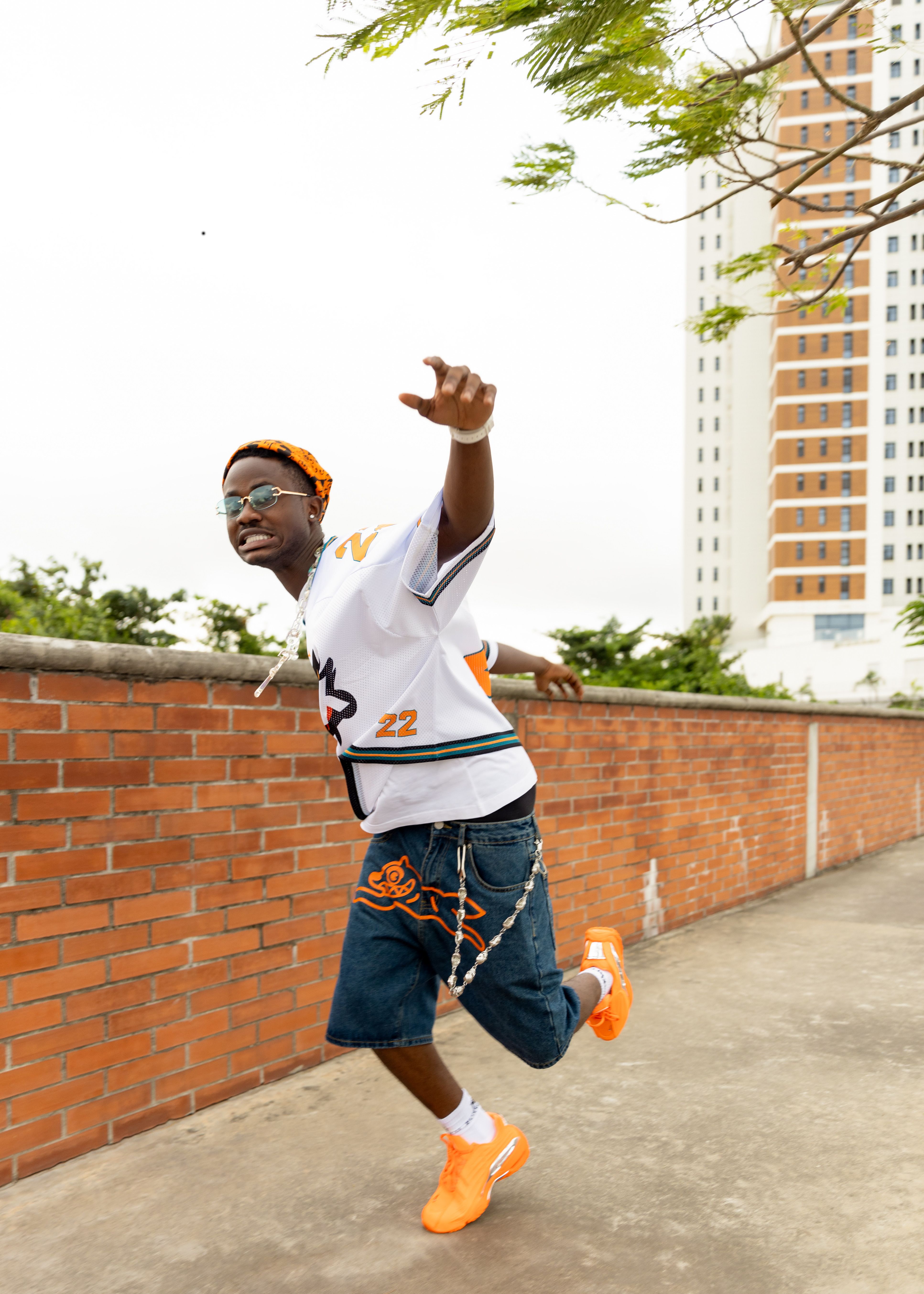 Energetic young man wearing casual streetwear running alongside a brick wall in an urban setting.