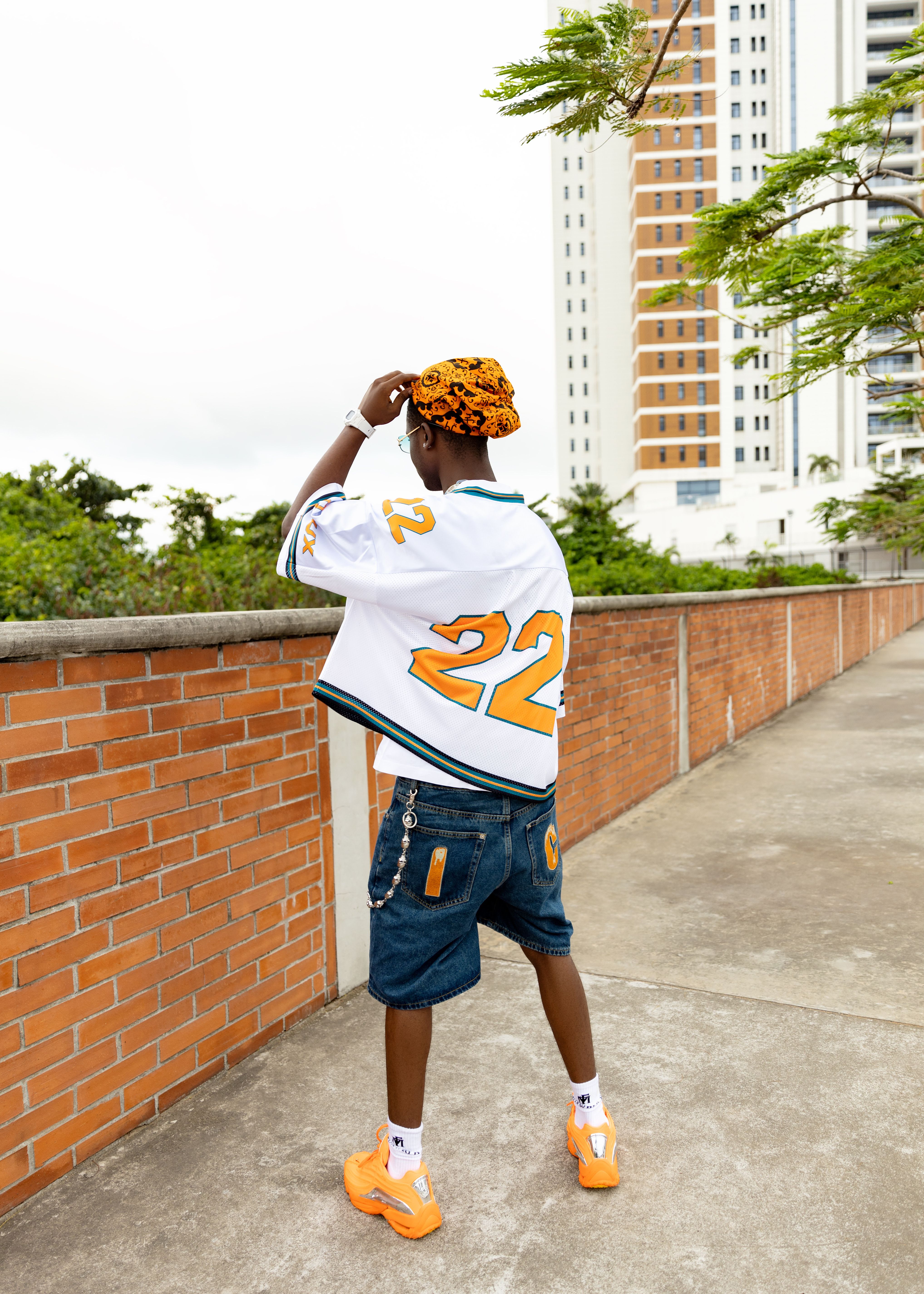 Stylish young man in a jersey and denim shorts walking by a cityscape with a tall building background.