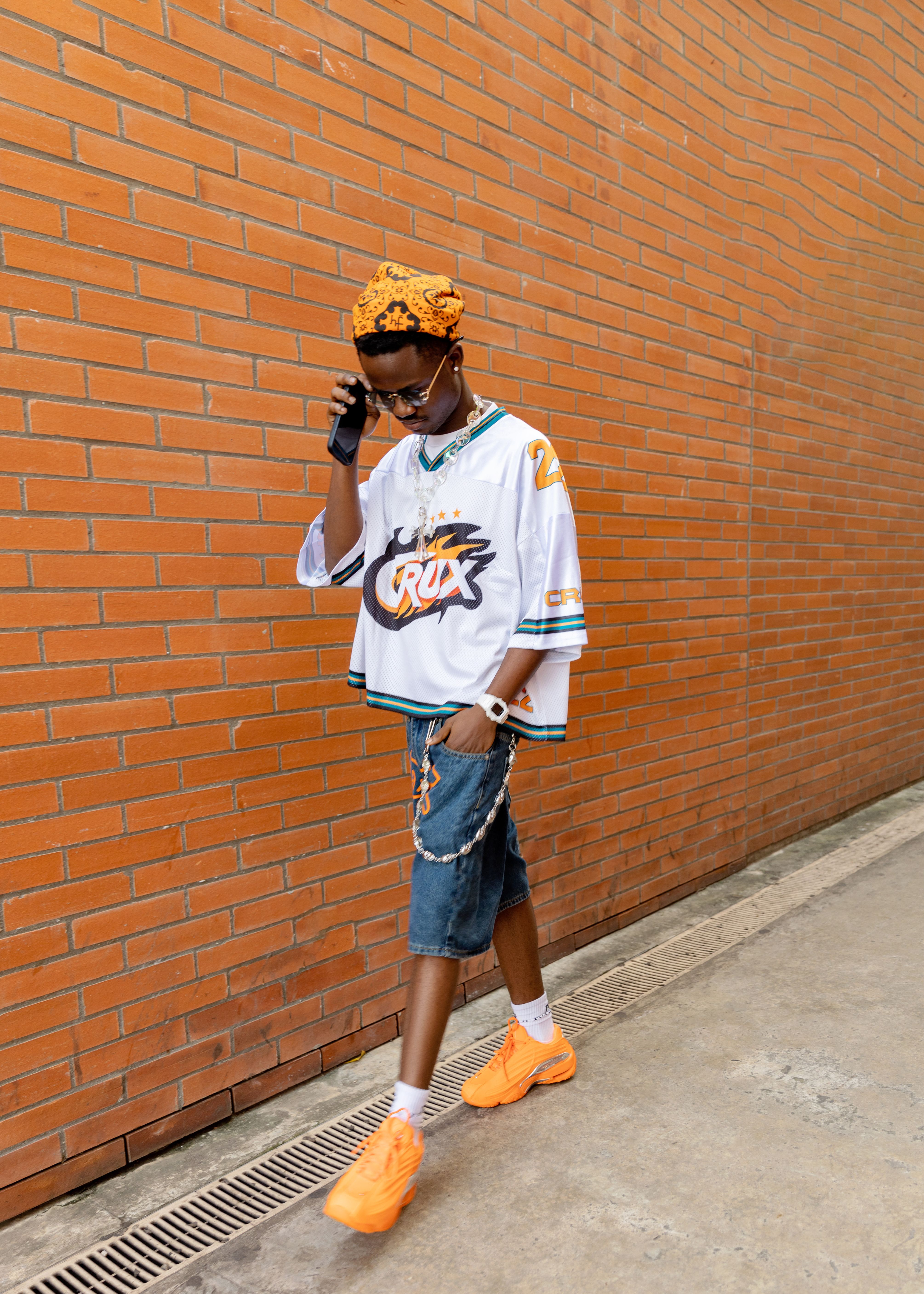 Stylish young adult in denim and jersey walking past a brick wall with casual confidence.