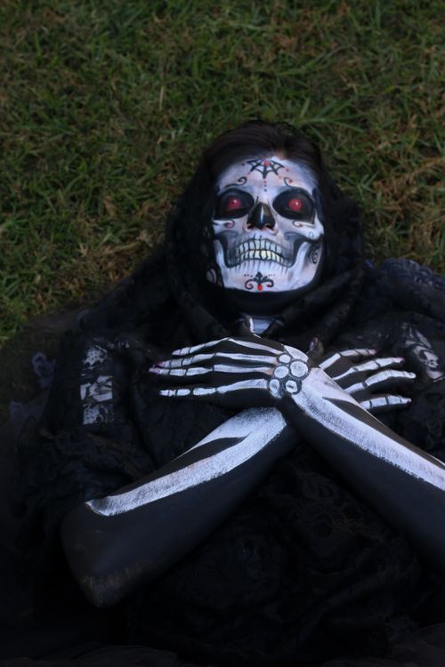Free Person with intricate skeleton makeup lying outdoors on grass, celebrating Day of the Dead. Stock Photo