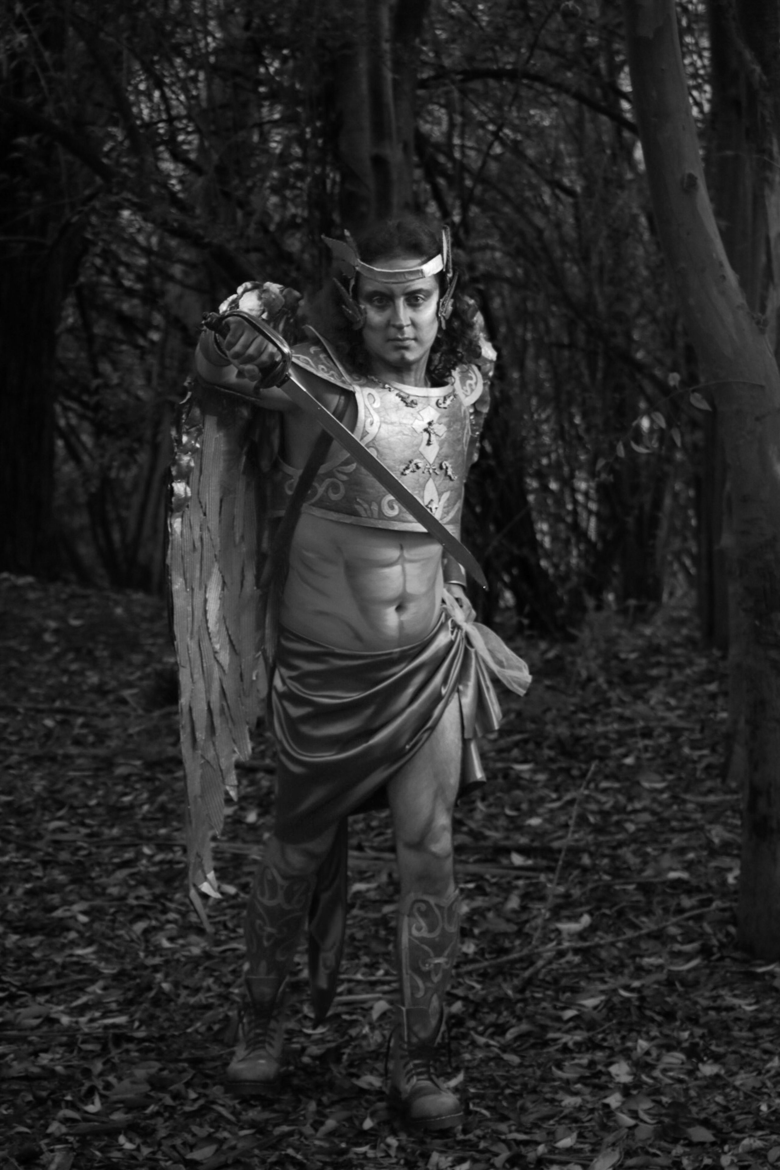 A male warrior in a fantasy costume holding a sword in a forest setting.