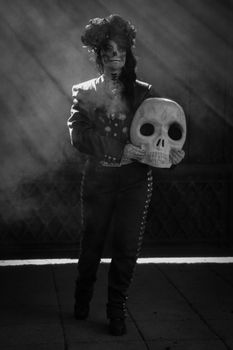 Person in Day of the Dead costume with face paint and skull prop in a dramatic black and white setting.