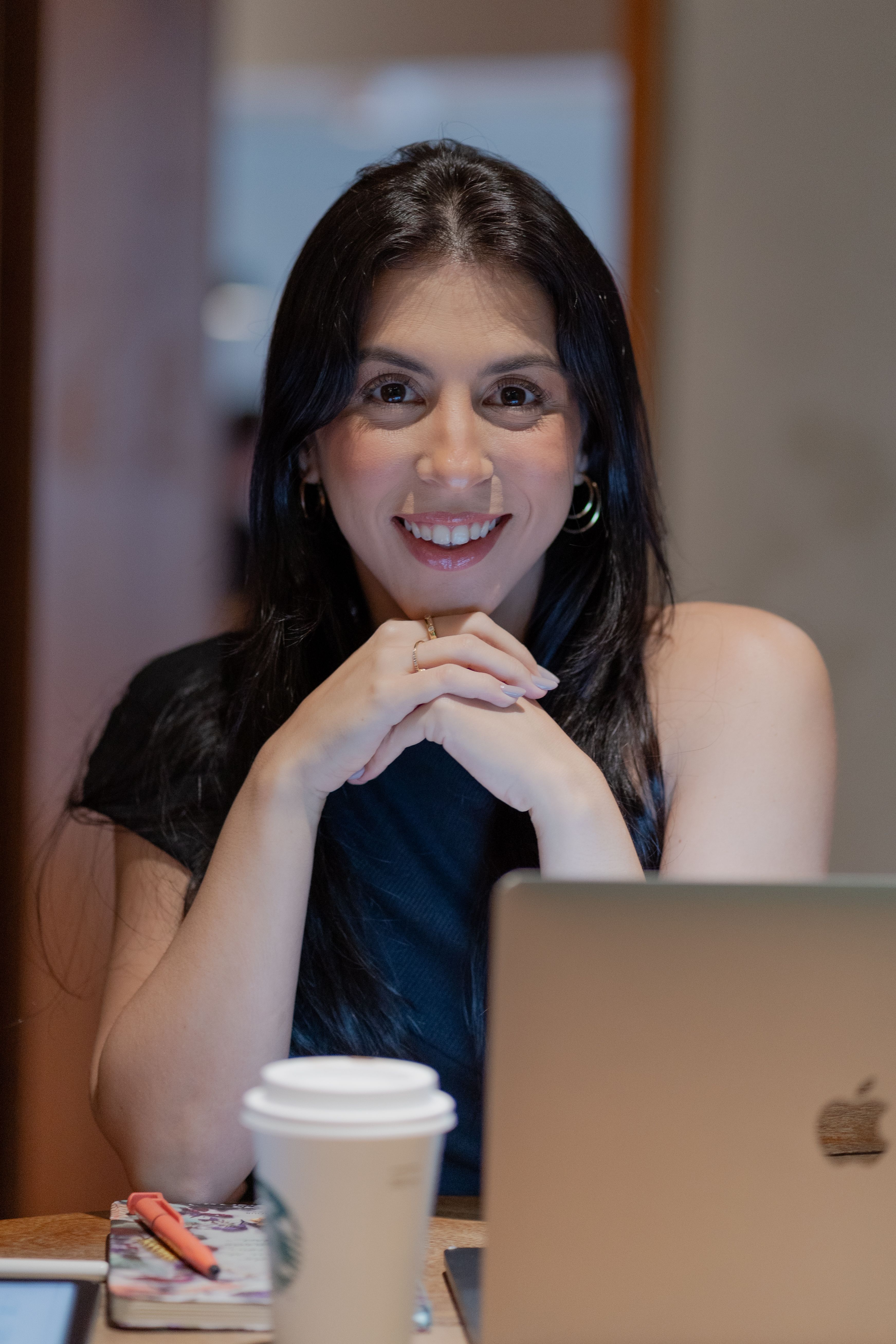 A person smiling and looking relaxed while working on a laptop in a sunny cafe