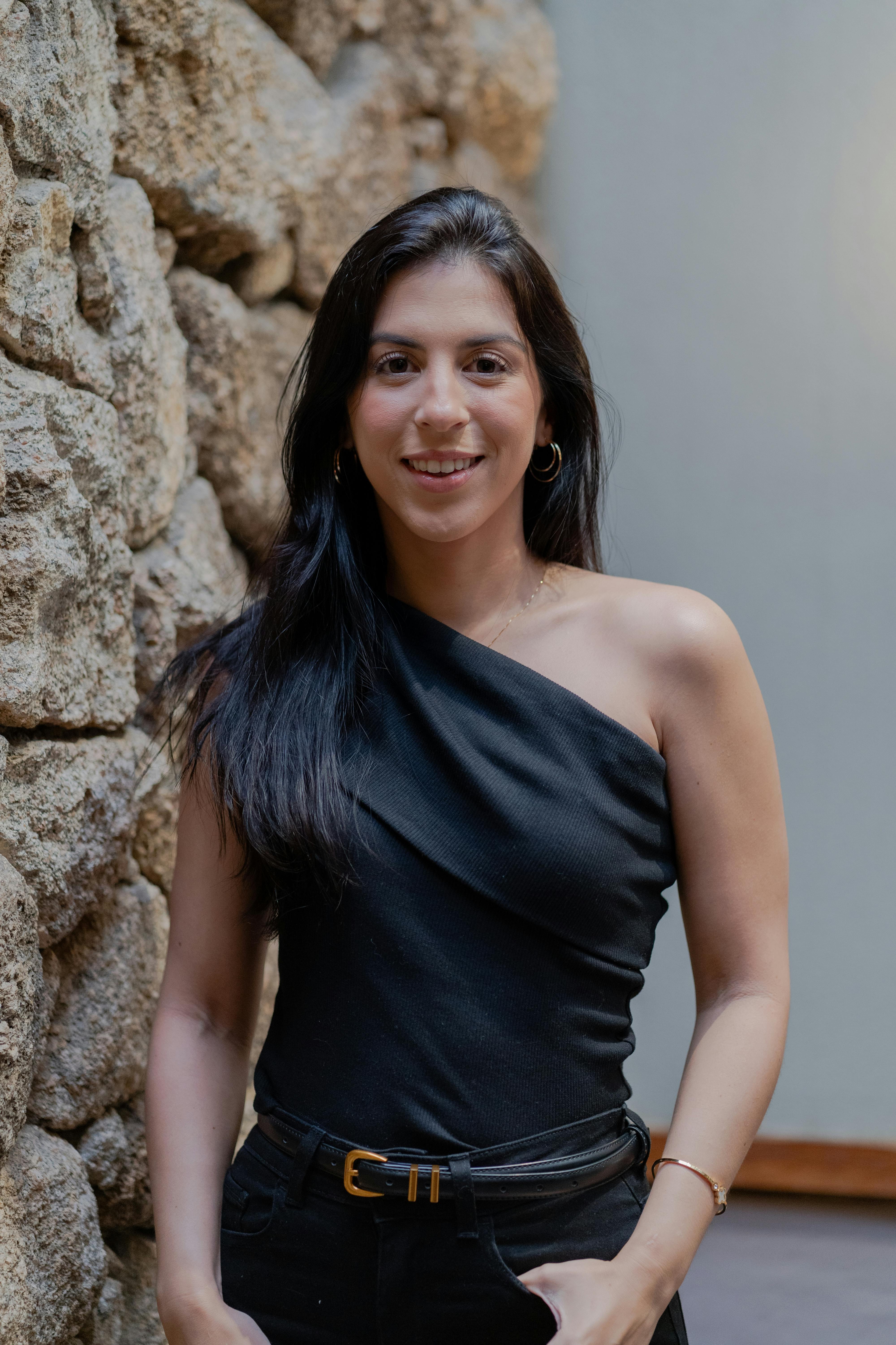 Woman in stylish black top posing by a rustic stone wall indoors.