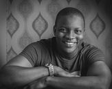 Black and white portrait of a smiling man leaning on his arms indoors.