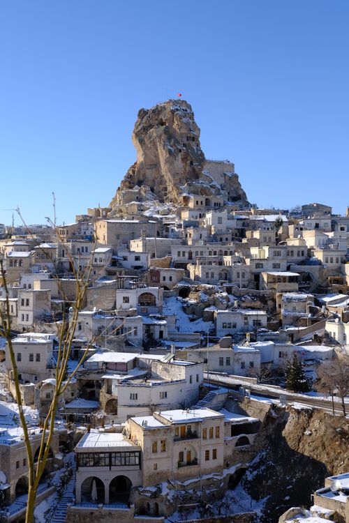 Free Snow-covered Uçhisar Castle with blue skies, showcasing unique Cappadocia architecture. Stock Photo