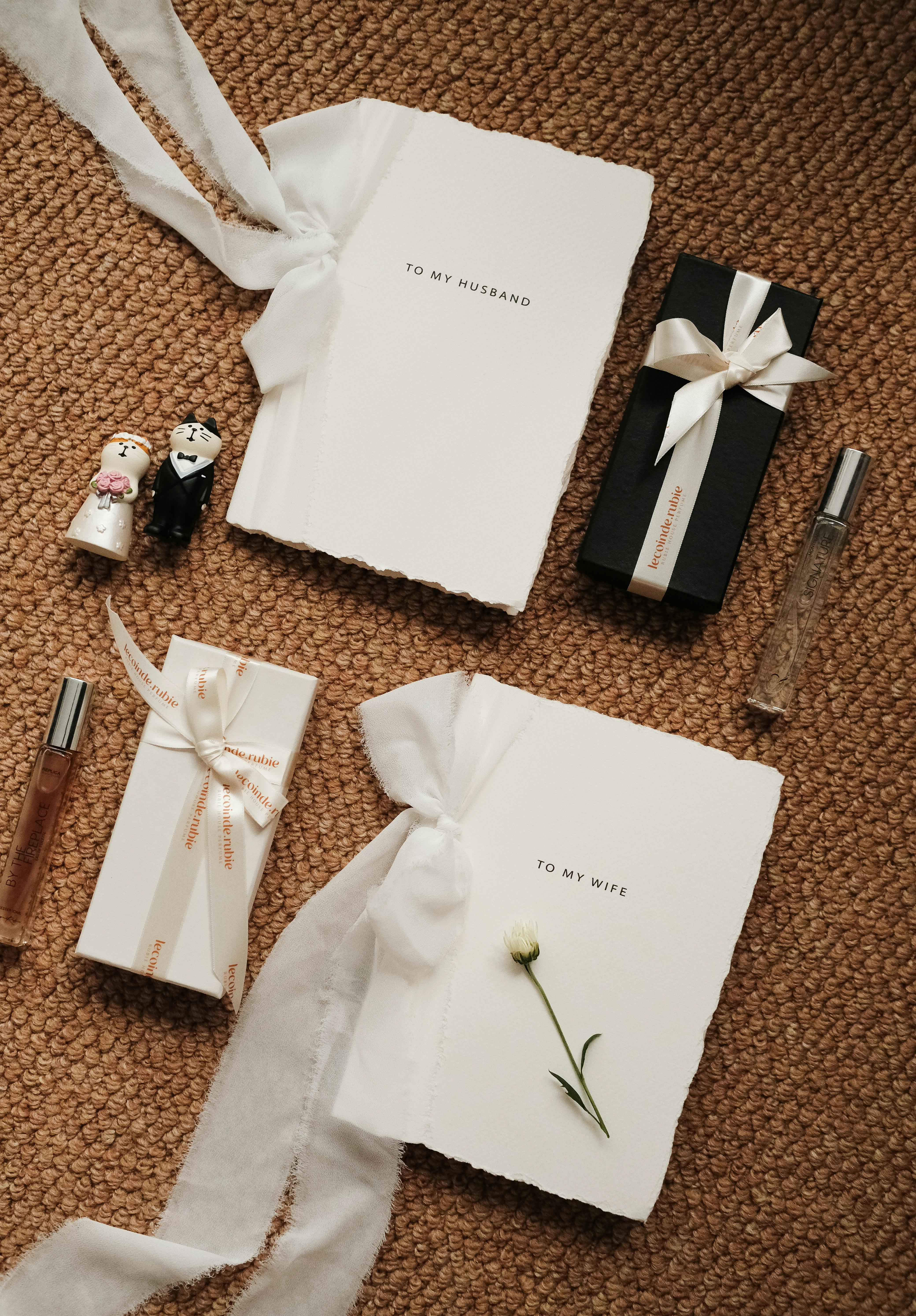 Stylish flat lay of wedding gifts with personalized notebooks and perfume on a textured background.