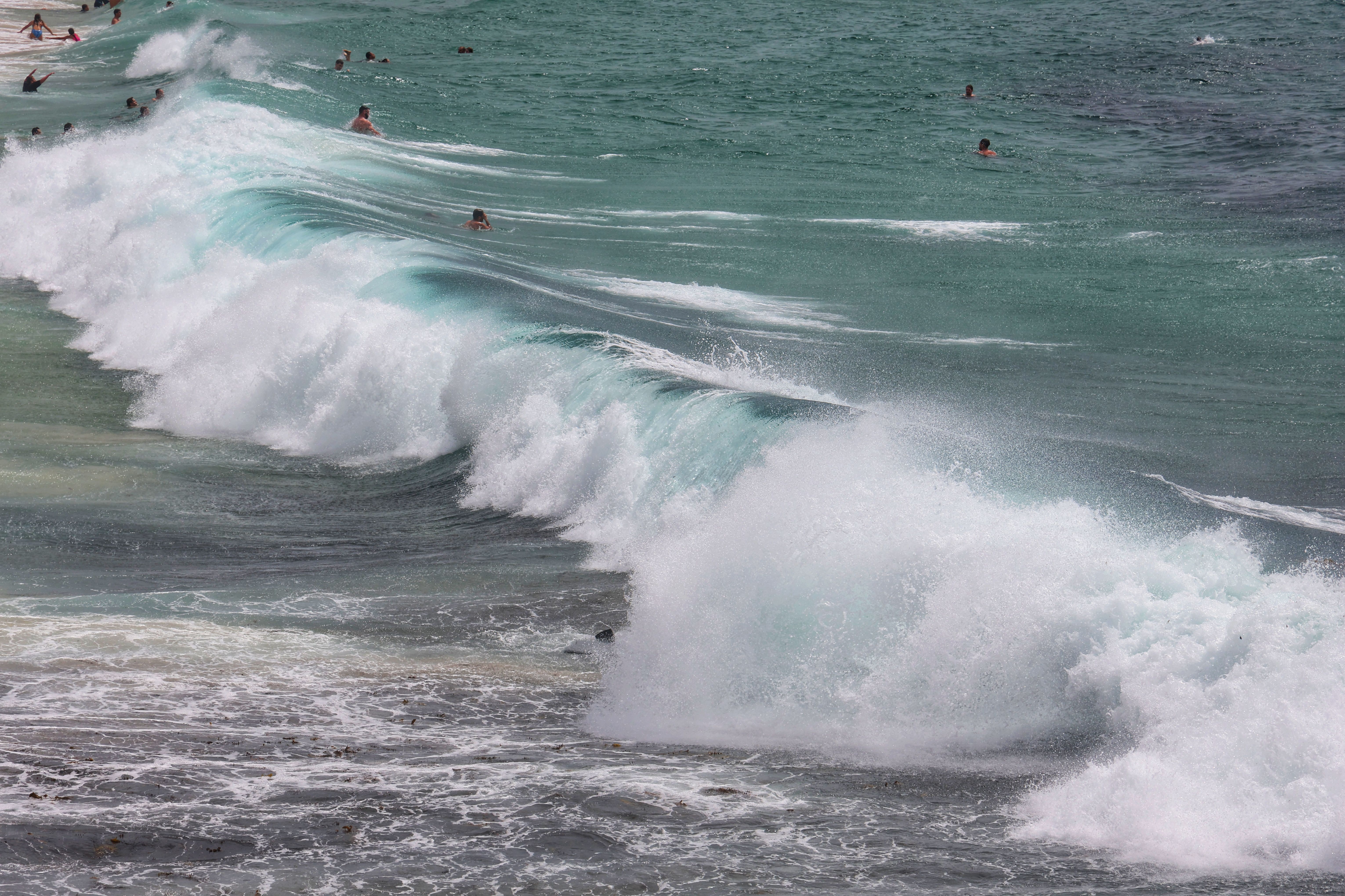 Dynamic ocean waves crashing on a beach with numerous swimmers enjoying the water.