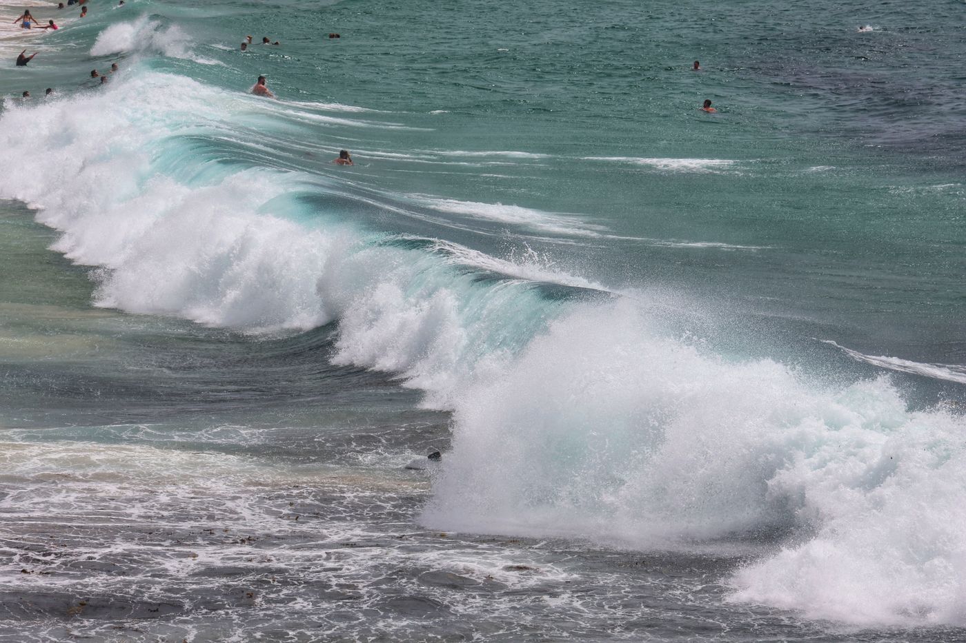 Dynamic ocean waves crashing on a beach with numerous swimmers enjoying the water.