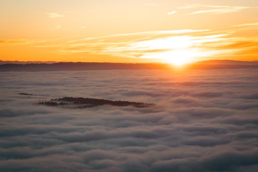A breathtaking view of the sun rising over a sea of clouds with a distant island, creating a serene and mystic atmosphere.