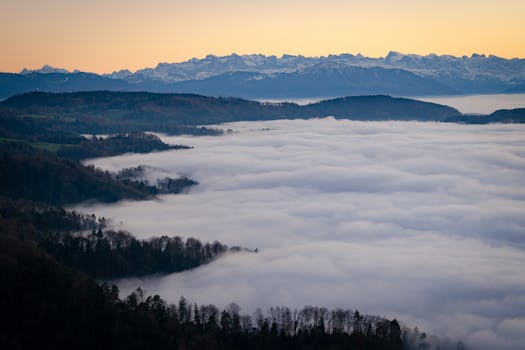 A breathtaking aerial view of fog draping over a mountain valley with distant peaks at sunrise.