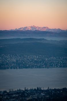 Scenic aerial view of Zurich cityscape with lakeside, Swiss Alps in the background at sunset.