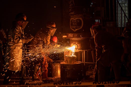 Workers engaged in metal casting in a foundry, with sparks flying from molten metal.