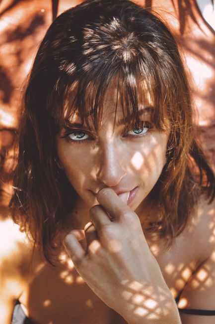 Captivating portrait of a woman with shadows and sunlight, expressing mystery and beauty.