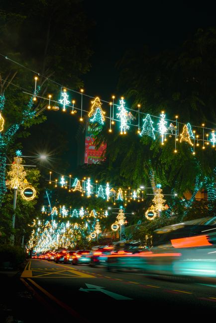 Fotomural Exposición prolongada de luces navideñas festivas y rastros de coches en un entorno urbano nocturno.