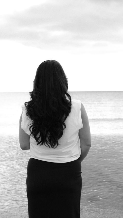Free A woman gazes at the ocean horizon in a serene black and white scene. Stock Photo