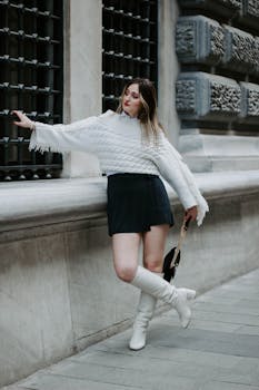 Fashionable woman in white boots posing confidently by a historic building in Istanbul.
