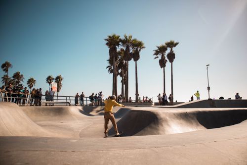 Free A skateboarder in yellow performs tricks at Venice Beach Skate Park under a clear blue sky. Stock Photo